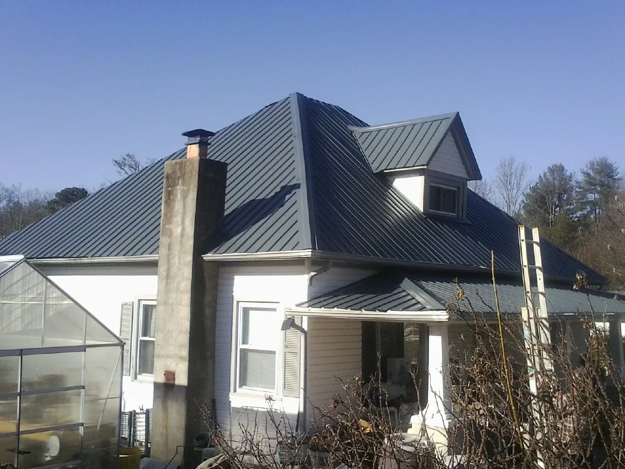 Dark blue standing seam metal roof on a white farmhouse with dormer — Slate & Tile Roof Repair by Roofing Brothers in Frostburg