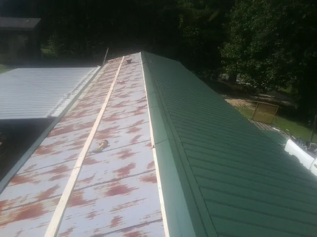Old rusted panels beside newly installed green metal roofing — Wind Damage Roof Repair by Roofing Brothers in Frostburg