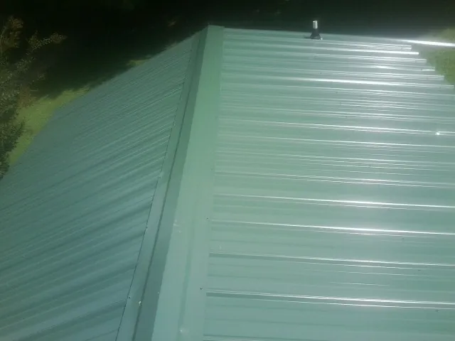 New green metal panels meeting at the ridge of a roof — Flat Roof Repair work by our crew in Frostburg