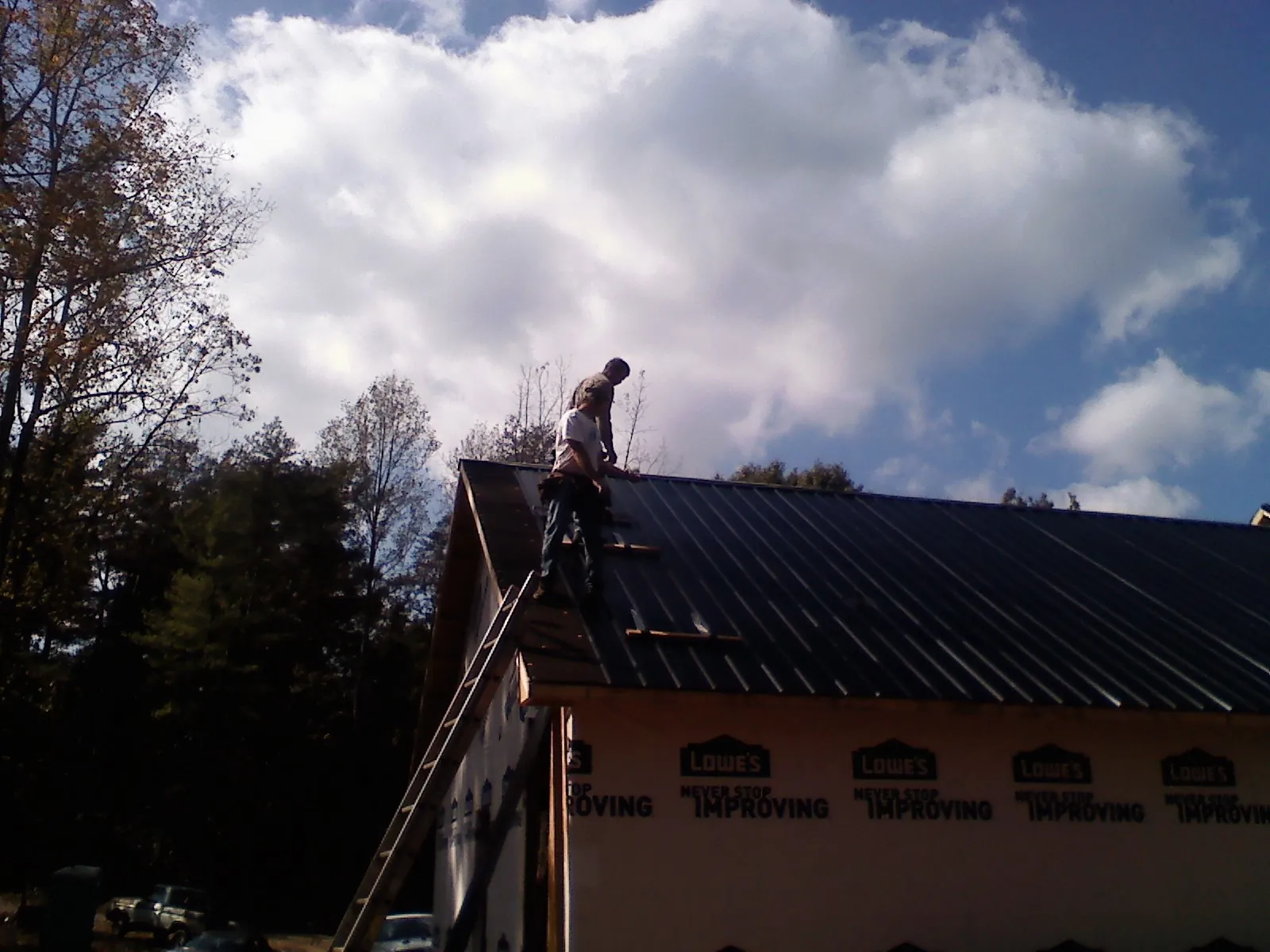 Roofer fastening dark metal panels high against a cloudy sky, from a Roof Inspection job in Frostburg