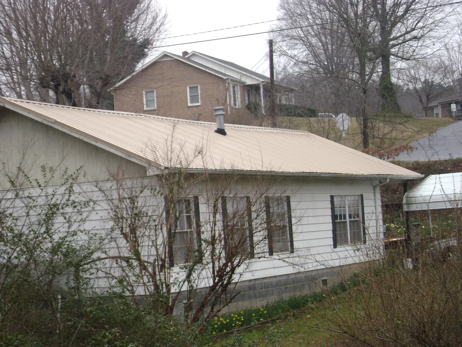 Tan metal roof on a white sided house set into a hillside — Commercial Roofing by Roofing Brothers in Frostburg
